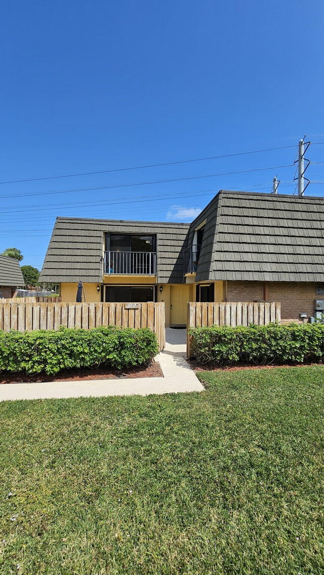 view of front of property with mansard roof, a front yard, fence, and stucco siding