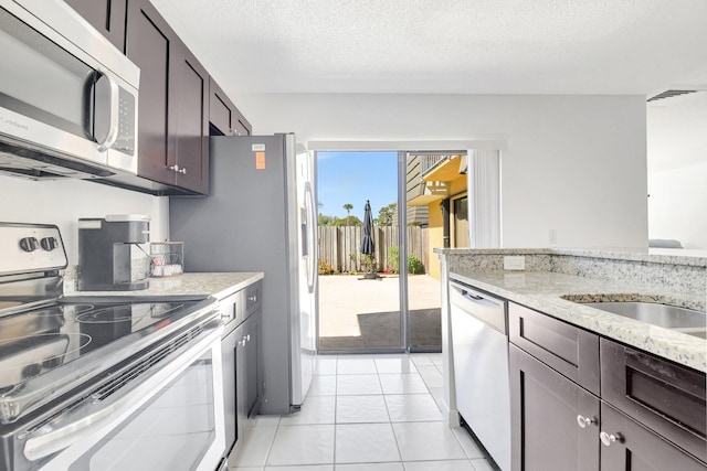 kitchen featuring dark brown cabinetry, light tile patterned floors, appliances with stainless steel finishes, light stone countertops, and a textured ceiling