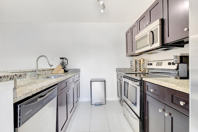 kitchen featuring light stone countertops, light tile patterned floors, a sink, dark brown cabinetry, and stainless steel appliances