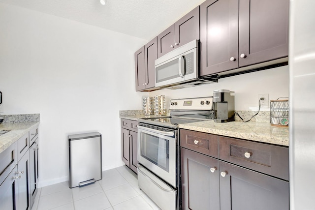 kitchen with light tile patterned floors, stainless steel appliances, dark brown cabinetry, a textured ceiling, and baseboards