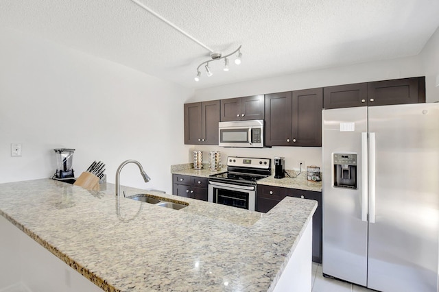 kitchen with stainless steel appliances, a sink, a textured ceiling, dark brown cabinetry, and a peninsula