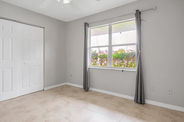 unfurnished bedroom with ceiling fan, a closet, light tile patterned flooring, and baseboards