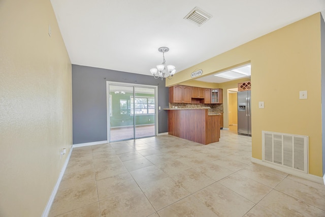 kitchen with brown cabinetry, stainless steel fridge, open floor plan, and visible vents