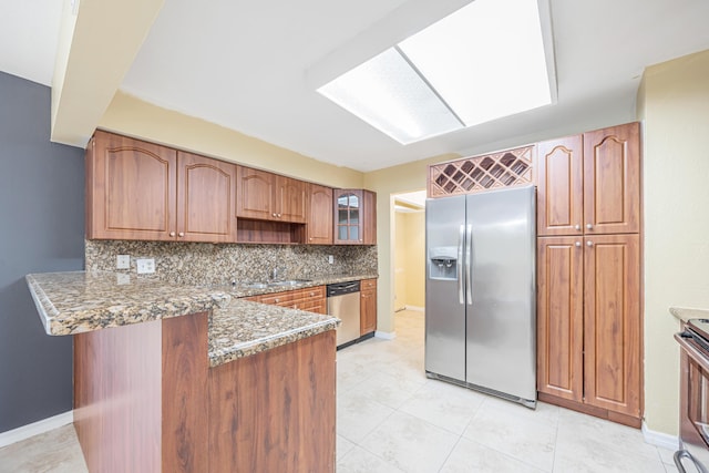 kitchen featuring decorative backsplash, appliances with stainless steel finishes, glass insert cabinets, dark stone countertops, and a peninsula