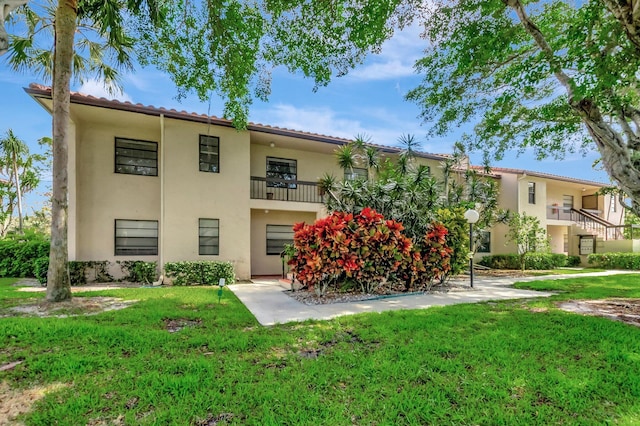 back of property with a lawn, a tile roof, and stucco siding