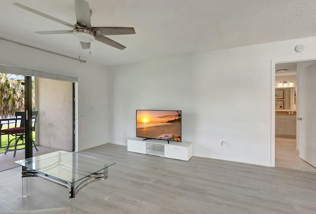 unfurnished living room with light wood-style floors, a textured ceiling, baseboards, and a ceiling fan