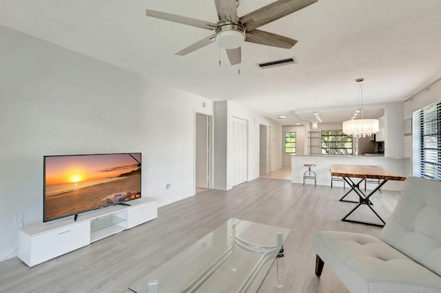 living room with light wood-style floors, visible vents, plenty of natural light, and ceiling fan with notable chandelier