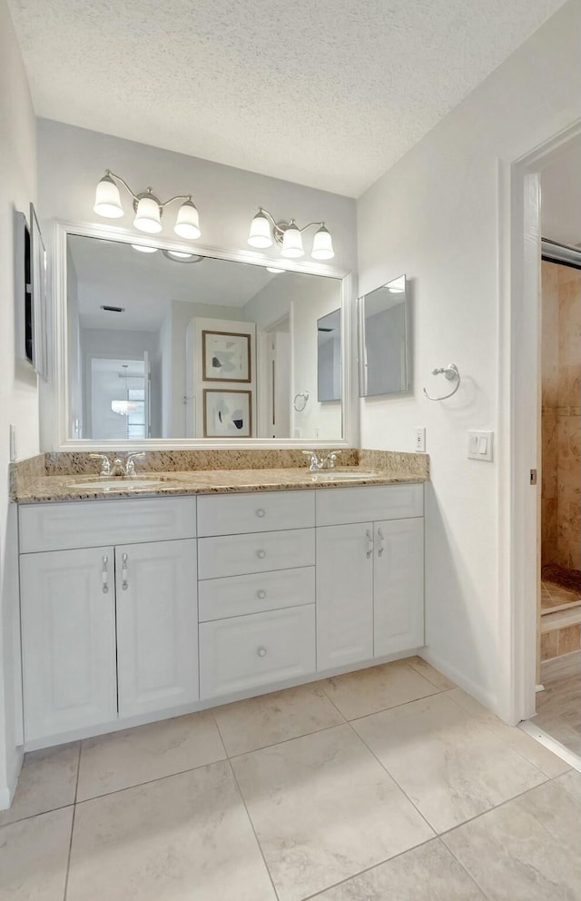 full bathroom with a textured ceiling, double vanity, walk in shower, and a sink