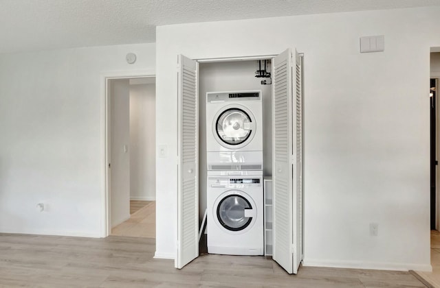 clothes washing area featuring laundry area, light wood-style flooring, a textured ceiling, and stacked washer and clothes dryer