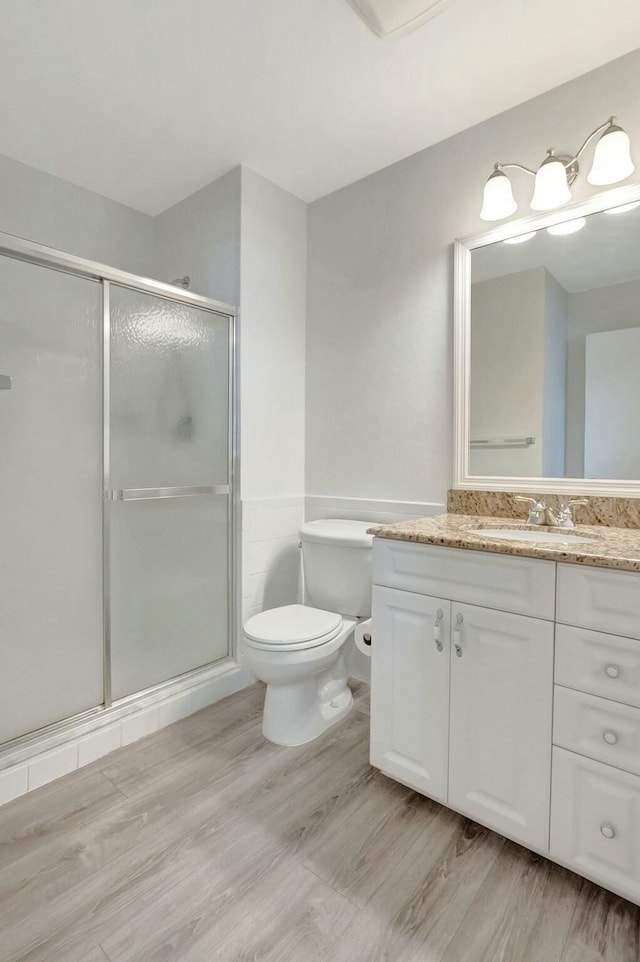 bathroom featuring toilet, a stall shower, wood finished floors, and vanity