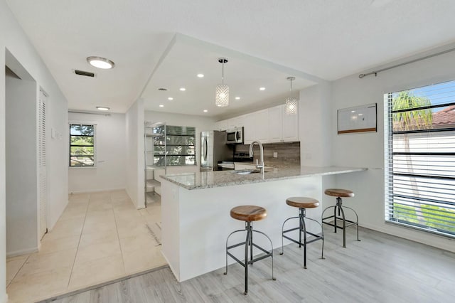 kitchen with appliances with stainless steel finishes, light stone counters, hanging light fixtures, a peninsula, and white cabinetry