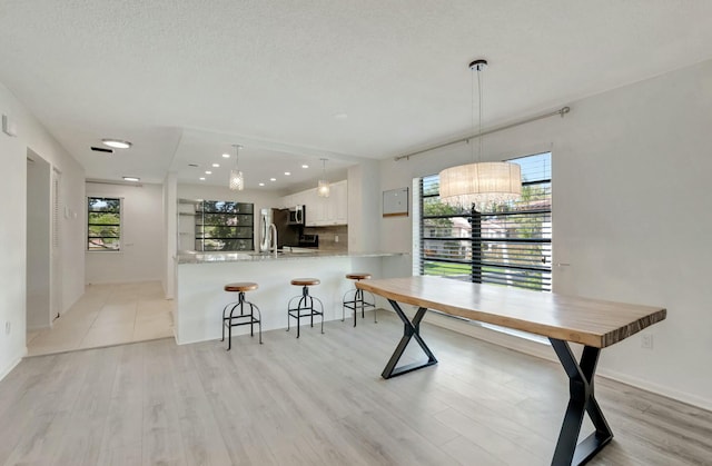 kitchen with light countertops, hanging light fixtures, light wood-style floors, white cabinets, and a peninsula