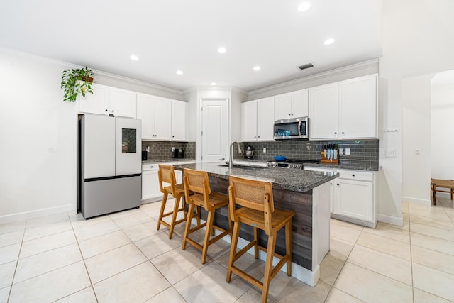 kitchen with an island with sink, a breakfast bar area, stainless steel microwave, dark stone countertops, and freestanding refrigerator