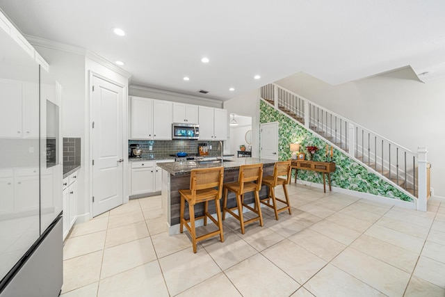 kitchen with white cabinets, dark stone counters, an island with sink, appliances with stainless steel finishes, and light tile patterned flooring