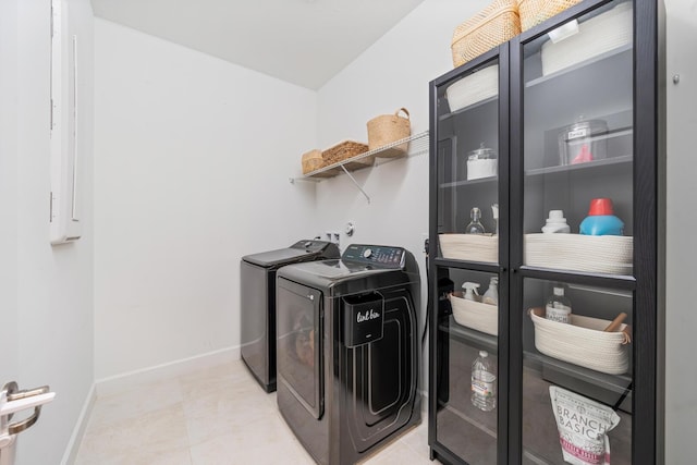 clothes washing area with light tile patterned floors, laundry area, washing machine and clothes dryer, and baseboards