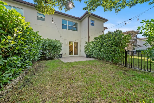 rear view of property with stucco siding, fence, a patio, and a lawn