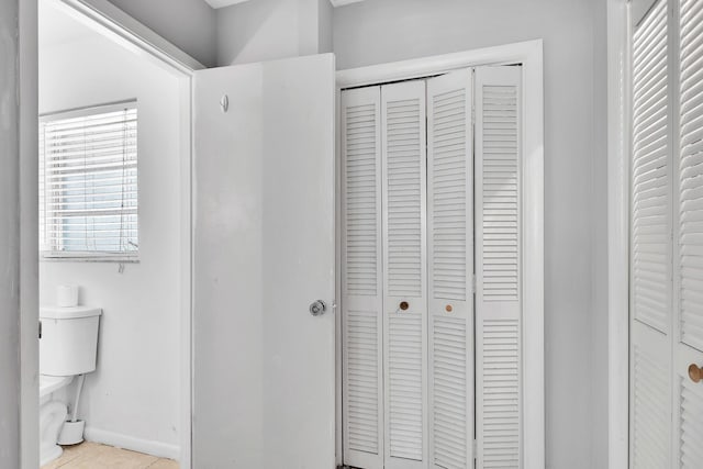 bathroom with a closet, tile patterned flooring, toilet, and baseboards