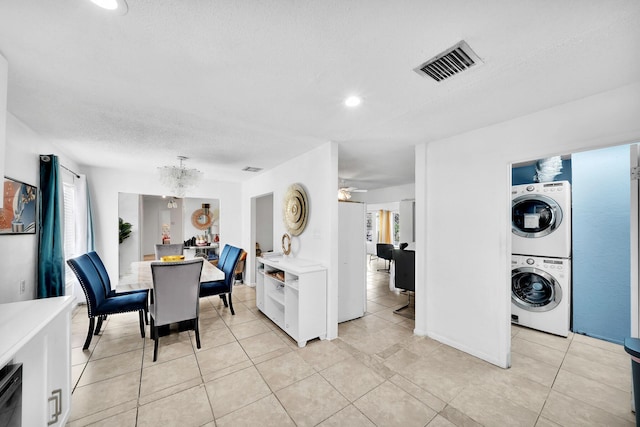 dining space featuring visible vents, ceiling fan with notable chandelier, a textured ceiling, stacked washing maching and dryer, and light tile patterned floors