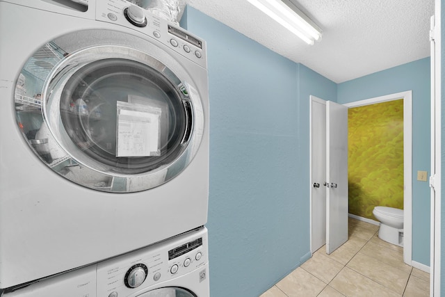 laundry room with stacked washer and clothes dryer, a textured ceiling, light tile patterned flooring, baseboards, and laundry area
