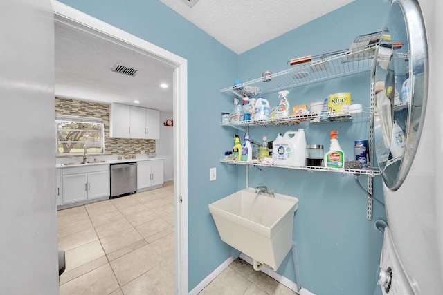 interior space featuring stainless steel dishwasher, a textured ceiling, white cabinetry, light tile patterned floors, and decorative backsplash