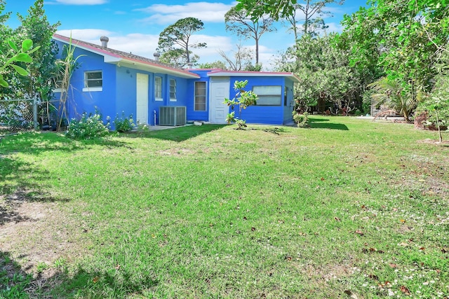 rear view of house featuring a lawn, fence, central AC, and stucco siding