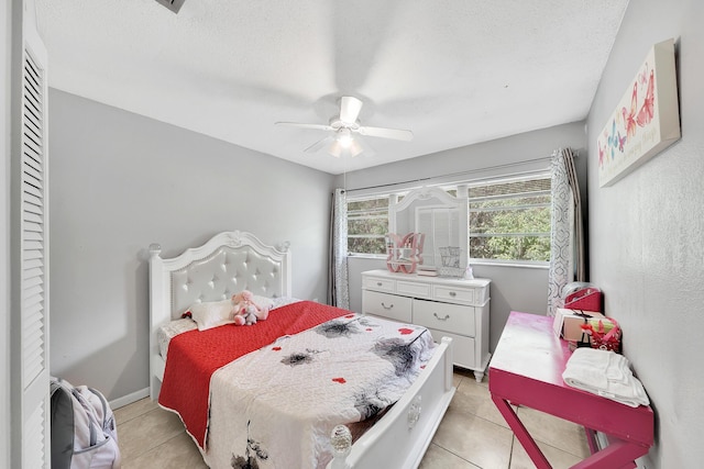 bedroom with light tile patterned floors, a ceiling fan, baseboards, and a textured ceiling