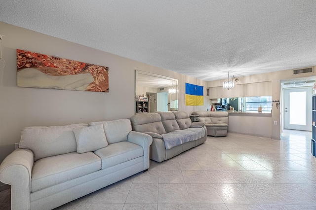 tiled living area featuring a textured ceiling, visible vents, and a notable chandelier