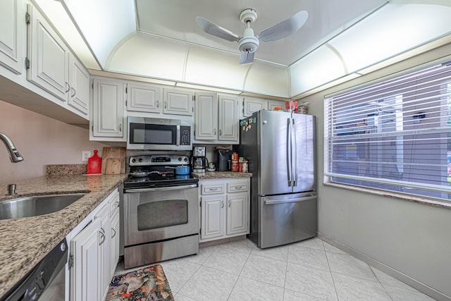 kitchen with light tile patterned floors, appliances with stainless steel finishes, a ceiling fan, a sink, and light stone countertops