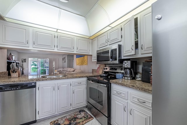 kitchen with white cabinets, glass insert cabinets, light stone counters, appliances with stainless steel finishes, and a sink