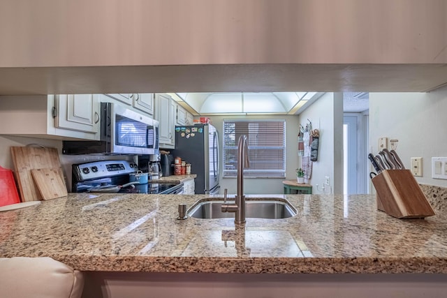 kitchen with a peninsula, a sink, white cabinetry, light countertops, and appliances with stainless steel finishes