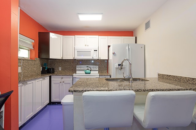 kitchen with a breakfast bar area, a peninsula, white appliances, visible vents, and white cabinets