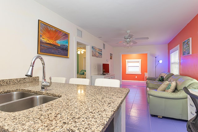 kitchen with light stone counters, a sink, visible vents, a ceiling fan, and open floor plan