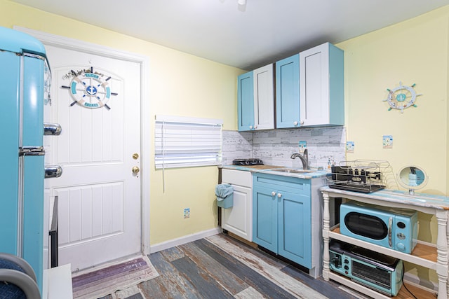 kitchen with dark wood-style flooring, light countertops, backsplash, a sink, and baseboards