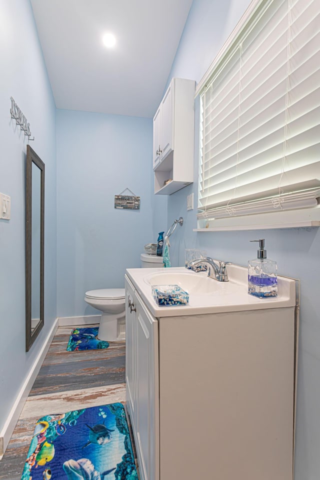 half bath with toilet, wood finished floors, vanity, and baseboards