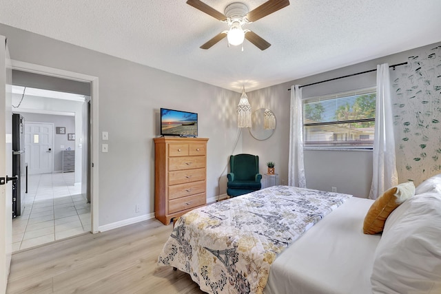 bedroom featuring baseboards, a textured ceiling, light wood-style flooring, and freestanding refrigerator