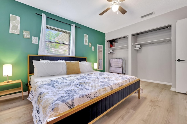 bedroom featuring a ceiling fan, baseboards, wood finished floors, visible vents, and multiple closets