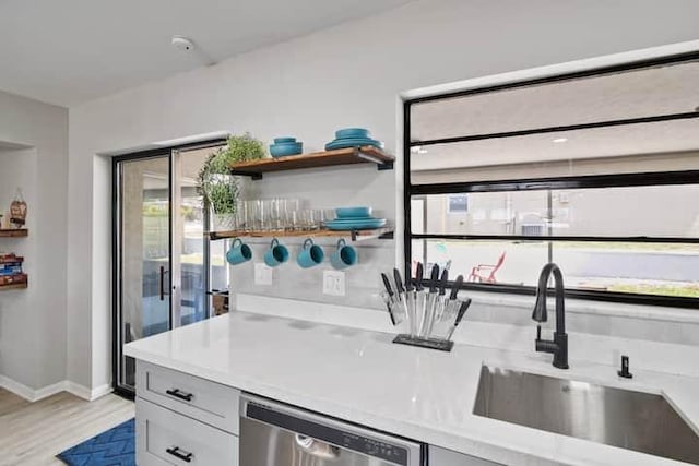 bar with stainless steel dishwasher, light wood-style flooring, baseboards, and a sink