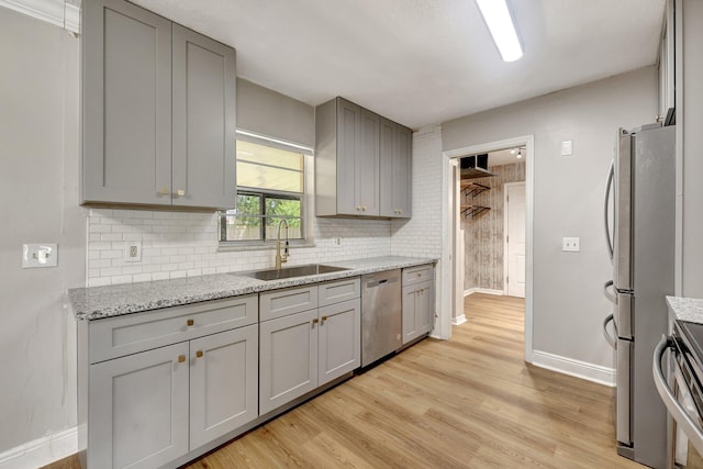 kitchen featuring backsplash, light wood-type flooring, gray cabinets, appliances with stainless steel finishes, and a sink