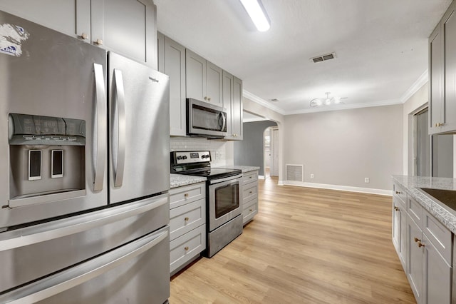 kitchen featuring visible vents, gray cabinetry, light wood-type flooring, arched walkways, and stainless steel appliances