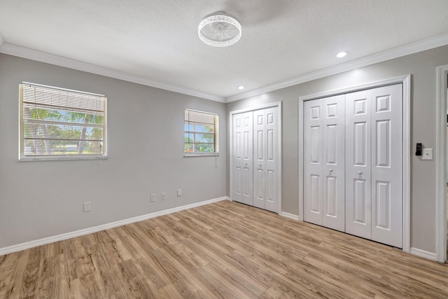 unfurnished bedroom featuring baseboards, light wood-style floors, multiple closets, a textured ceiling, and crown molding