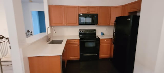 kitchen featuring black appliances, a peninsula, a sink, and light countertops