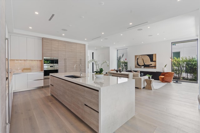 kitchen featuring tasteful backsplash, light wood-style flooring, double oven, a sink, and modern cabinets