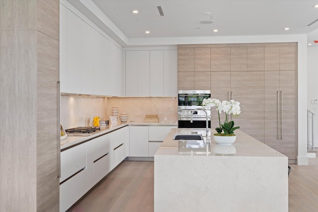 kitchen with appliances with stainless steel finishes, an island with sink, modern cabinets, and a sink