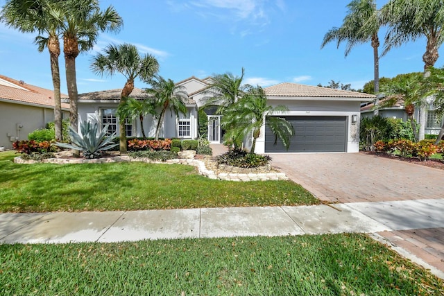 ranch-style house featuring decorative driveway, stucco siding, an attached garage, a front yard, and a tiled roof