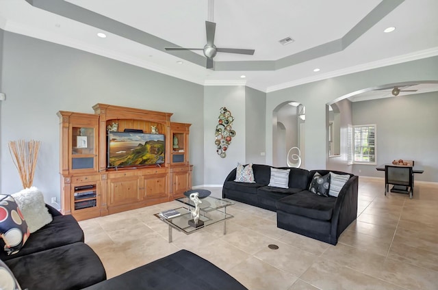 living area with a tray ceiling, arched walkways, light tile patterned floors, visible vents, and a ceiling fan