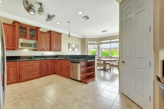 kitchen with dark countertops, ornamental molding, a peninsula, stainless steel appliances, and a sink