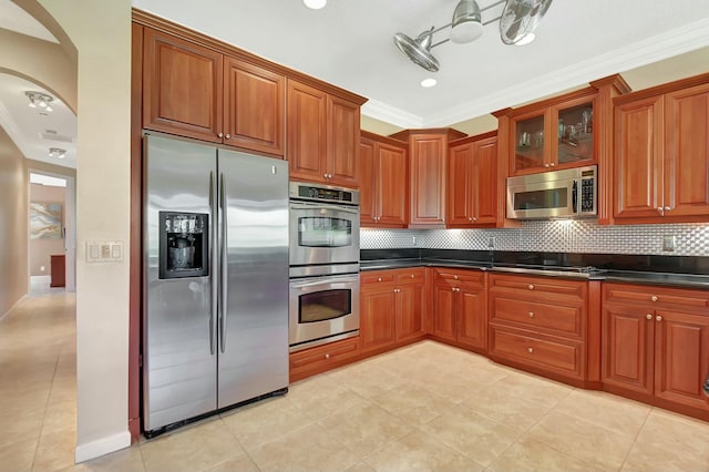 kitchen featuring appliances with stainless steel finishes, arched walkways, dark countertops, and decorative backsplash