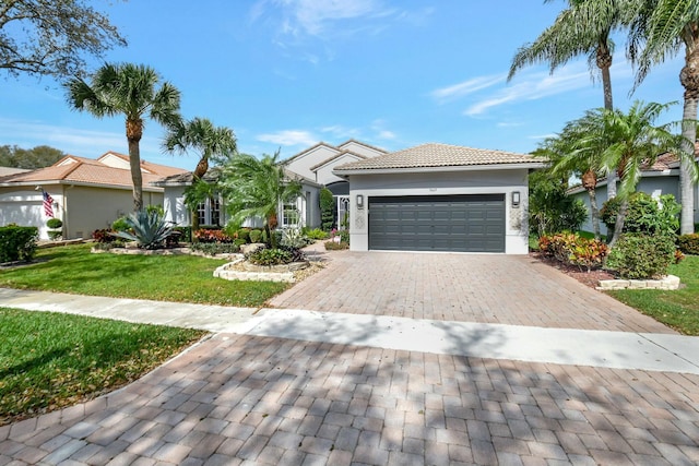 view of front of home featuring a tiled roof, an attached garage, decorative driveway, a front lawn, and stucco siding