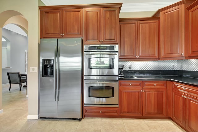 kitchen with stainless steel appliances, arched walkways, backsplash, and dark countertops