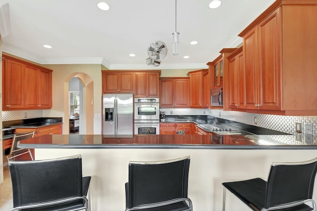 kitchen with stainless steel appliances, dark countertops, brown cabinetry, and a peninsula